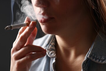 Woman in shirt smoking cigarette on dark background, closeup. Bad habit