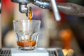 Close-up of a glass of freshly prepared creamy latte with latte art on top, served on a dark wooden table in a cozy coffee shop atmosphere, with blurred background