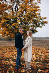 A couple hugging under a yellow-leaved autumn tree. Romantic walk in the fall park, warm atmosphere, love, and harmony surrounded by colorful foliage.