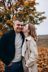 Fototapeta premium Romantic couple embracing under an autumn tree. Lovers stand among fallen yellow leaves, enjoying a tender moment in nature. Romantic moment surrounded by nature and fallen leaves. vibrant autumn tree
