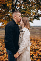 Romantic couple embracing under an autumn tree. Lovers stand among fallen yellow leaves, enjoying a tender moment in nature. Romantic moment surrounded by nature and fallen leaves. vibrant autumn tree