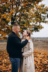 A couple hugging under a yellow-leaved autumn tree. Romantic walk in the fall park, warm atmosphere, love, and harmony surrounded by colorful foliage.