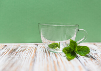 Tea cup with fresh mint leaves on a table on a green background with copy space. Health benefits of peppermint tea concept.