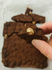 Hand holding a piece of homemade chocolate with hazelnuts