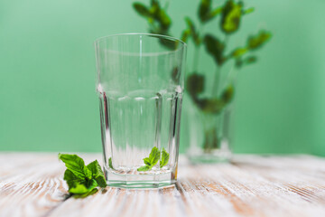 A glass with fresh mint leaves water on a table on a green background with copy space. Health benefits of peppermint water  concept.