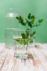 A glass with fresh mint leaves water on a table on a green background with copy space. Health benefits of peppermint water  concept.