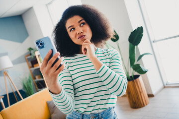 Young woman with vibrant personality using smartphone in modern living room with striped shirt, stylish interior, and cozy sofa
