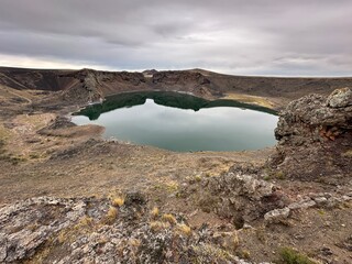 A stunning natural lagoon formed inside the crater of an ancient volcano, surrounded by dark volcanic rock. This unique geological landscape showcases raw natural beauty and dramatic terrain, perfect 