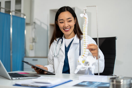 Doctor explains spine surgery using anatomical model in medical office.