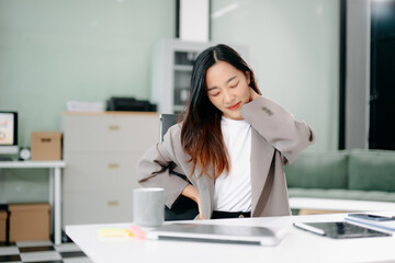 Overworked young Asian businesswoman office worker suffering from neck pain after had a long day at her office desk.