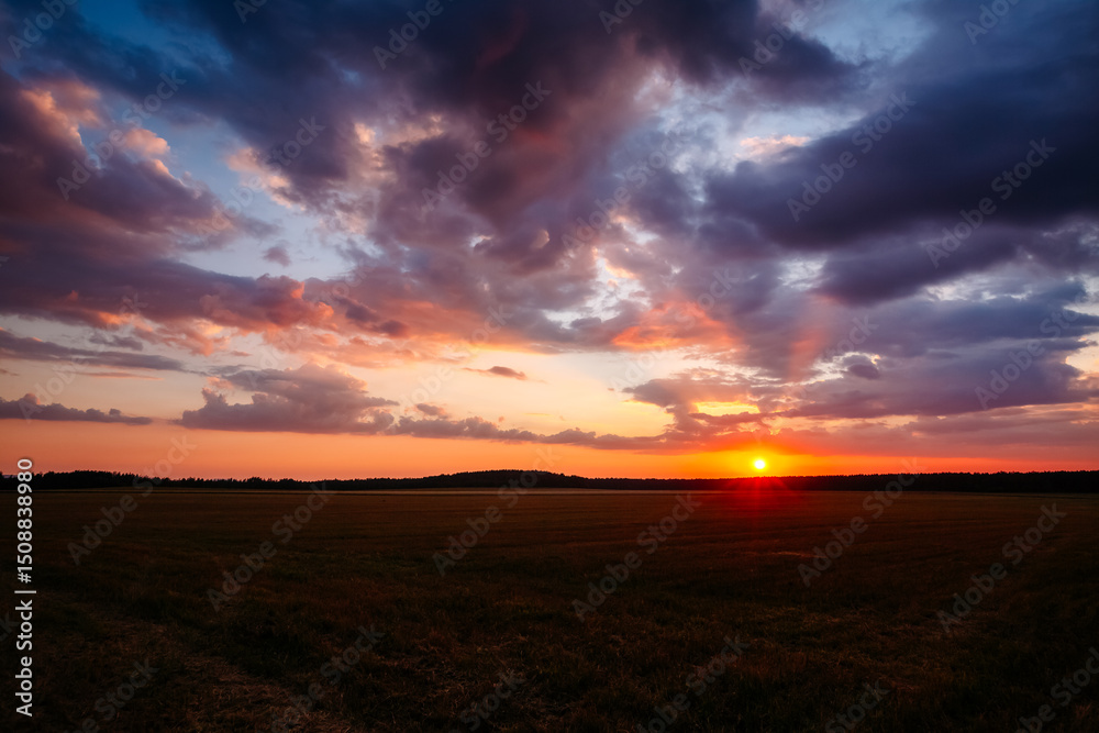 Poster gorgeous sunset over an open field with colorful clouds in the dark evening sky.