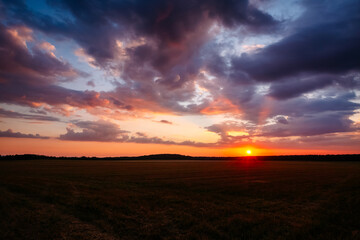 Gorgeous sunset over an open field with colorful clouds in the dark evening sky.