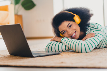 Young woman with headphones relaxing in a cozy living room beside a laptop, enjoying music and...