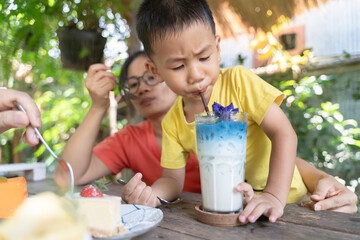 Young boy sipping a colorful butterfly pea milk drink from a tall glass with ice, surrounded by...