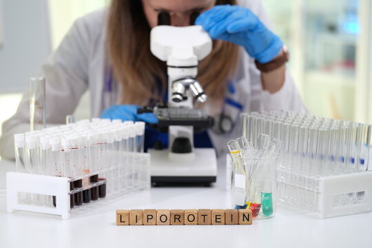 A scientist is using a microscope to conduct detailed lipoprotein research, surrounded by test tubes and samples