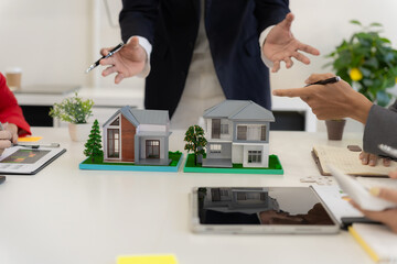 Real estate agent with client signing contract, money and documents on table with model home...