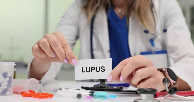 Woman doctor explains symptoms of lupus to patient. Physician shows card with word Lupus and speaks about importance of early diagnosis at appointment