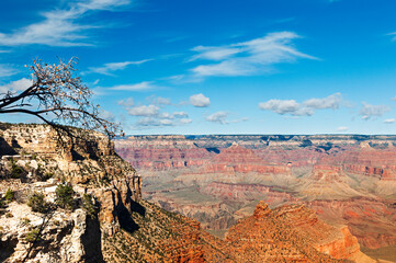 A breathtaking view of the Grand Canyon, showcasing its vastness and layered rock formations under a bright blue sky with scattered clouds. 
