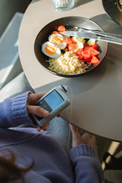 Overhead view of a woman sitting at a table injecting insulin with an insulin pump before a meal
