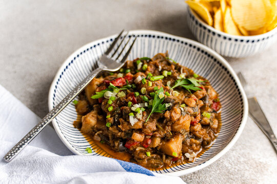 Close-up of a Traditional Georgian chicken and tomato chakhokhbili dish with a bowl of ridged potato crisps