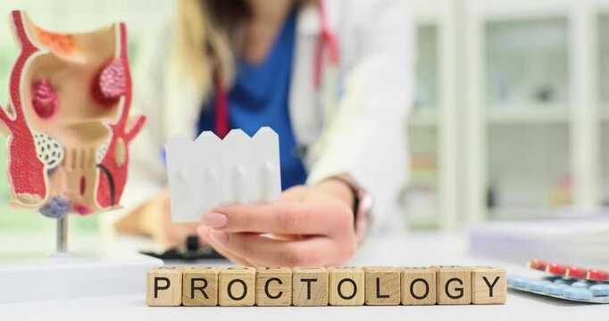 Woman proctologist shows set of suppositories by word Proctology on desk. Doctor discusses symptoms of anal fissures and holds appropriate medication