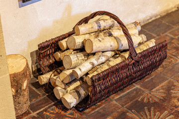Rustic wooden basket filled with birch logs on tiled floor