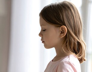 Profile of a young girl with light brown hair, looking thoughtfully towards a window