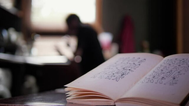 A man is practicing martial arts moves, appearing to train in front of a book titled "Kung Fu" that is open on a table. The background suggests an indoor setting with natural light