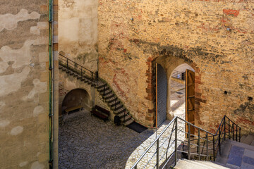 Historic stone courtyard with arched doorway and staircases in sunlight