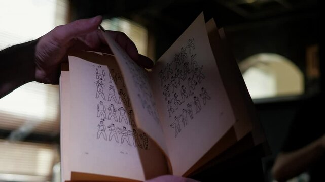 An open book about Kung Fu training is displayed on a wooden surface, showing illustrations of martial arts poses or techniques. The pages appear well-used, suggesting frequent study or practice