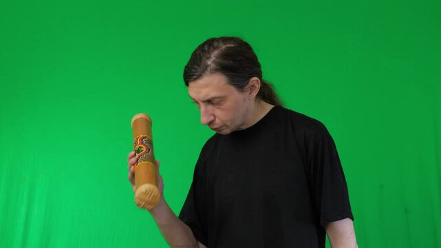 A man with a thoughtful expression holds and inspects a didgeridoo against a vibrant green screen, providing ample space for custom backgrounds