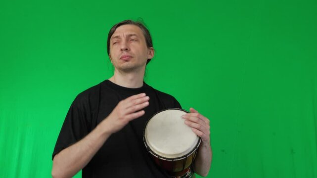A man demonstrates playing a djembe drum against a vivid green screen background, perfect for compositing with various settings and themes