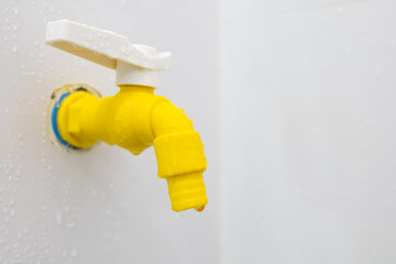 Yellow plastic faucet mounted on the wall in the bathroom