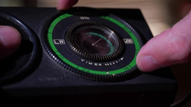 A hand holds a classic portable radio with a prominent tuning dial and speaker, set against a dark, moody background, suggesting nostalgia or a signal search
