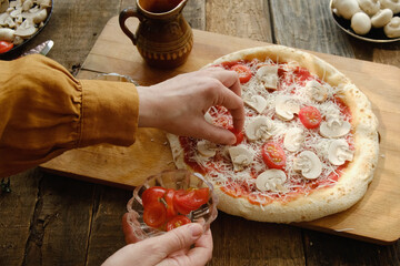 Making pizza. Female hands put sliced tomatoes on the dough