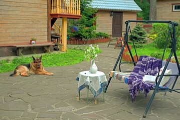 Apple blossoms on a table in front of a sofa swing in the courtyard of a country house.