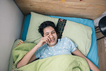 Teenager girl waking up and rubbing her eyes in bed in the morning