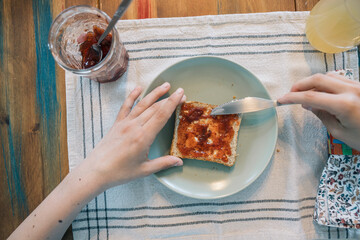 Hands of unrecognizable person spreading strawberry jam on toast for breakfast
