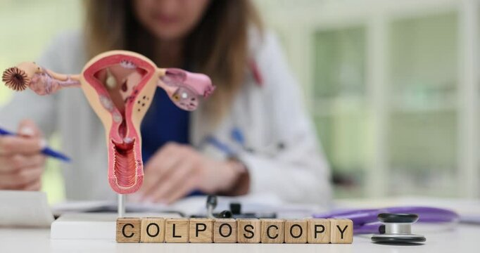 Text Colposcopy on wooden blocks and uterus model for education on desk. Woman doctor documents gynecological examination on clinical workspace