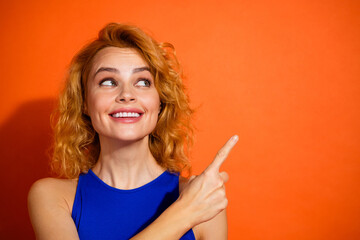 Smiling young woman pointing upward, showcasing vibrant red hair and blue top against a bold orange...