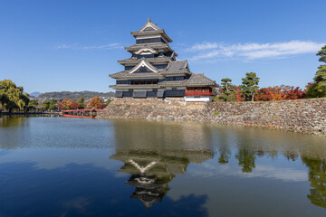 Obraz premium Historic Matsumoto Castle in Nagano with its multi-tiered black walls mirrored perfectly in the still moat water during sunny autumn weather