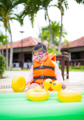 Cute little Asian girl wearing life jacket playing in swimming pool,Asian girl wearing life jacket...