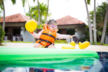 Cute little Asian girl wearing life jacket playing in swimming pool,Asian girl wearing life jacket...