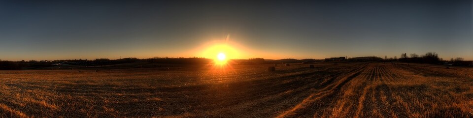 Golden sunset light over a rural farm field with hay bales and stubble. Panoramic view of agricultural land during harvest season.