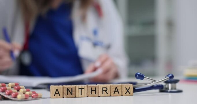 Word Anthrax on wooden cubes with pills and stethoscope in clinic office. Woman healthcare worker writes documenting infectious disease diagnosis