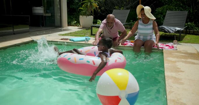 Diverse grandparents enjoying pool time with granddaughter on inflatable donut float