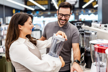 Smiling shop assistant helping a pregnant customer choose home appliances while showcasing various products in a vibrant electronics store