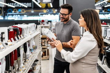 Smiling shop assistant helping a pregnant customer choose home appliances while showcasing various products in a vibrant electronics store