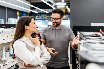 Smiling shop assistant helping a pregnant customer choose home appliances while showcasing various products in a vibrant electronics store