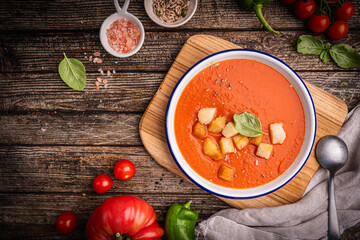 Gazpacho soup in bowl with ingredients over wooden background. Cold tomato soup. Healthy food concept. Top view, flat lay. High quality photo